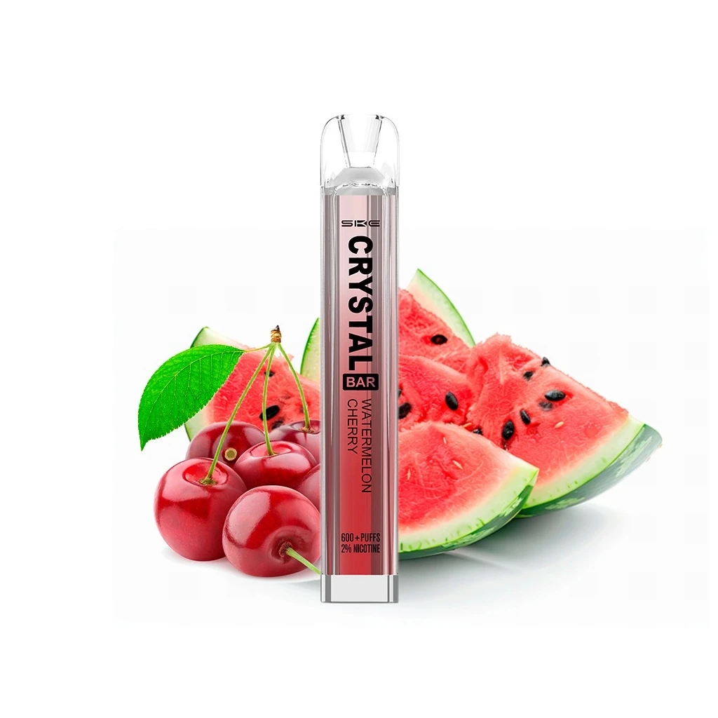 Vapeador SKE Crystal Bar Watermelon Cherry con boquilla transparente y etiqueta rosa, delante de cerezas y rodajas de sandía. Vapeador SKE Crystal Bar Watermelon Cherry con boquilla transparente y etiqueta rosa, delante de cerezas y rodajas de sandía.