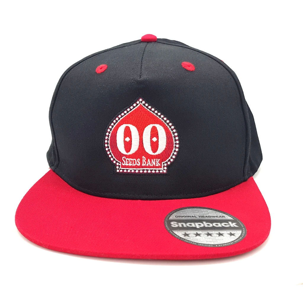 Gorra negra 00 Seeds con visera plana roja, bordado frontal rojo y blanco, y pegatina circular sobre la visera.