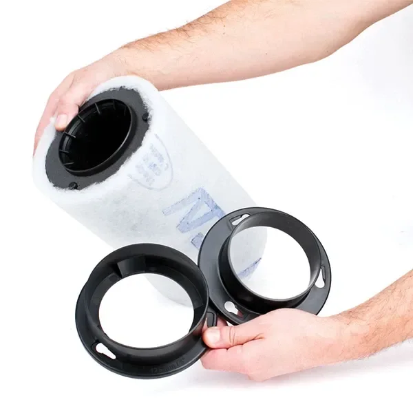 Unas manos sostienen un filtro cilíndrico con funda blanca y manguitos negros con rebordes y orificios, sobre fondo blanco.