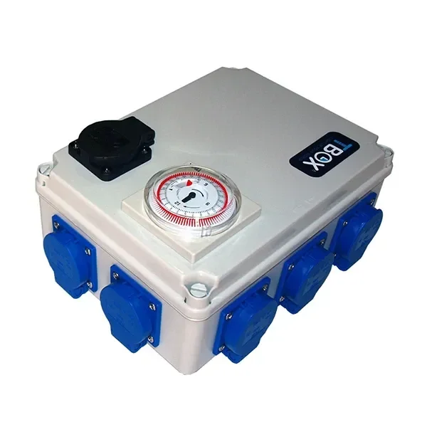 Temporizador TBOX en caja gris vista en perspectiva, con dial analógico en la tapa, una toma negra superior y varias tomas azules laterales. Temporizador TBOX en caja gris vista en perspectiva, con dial analógico en la tapa, una toma negra superior y varias tomas azules laterales.