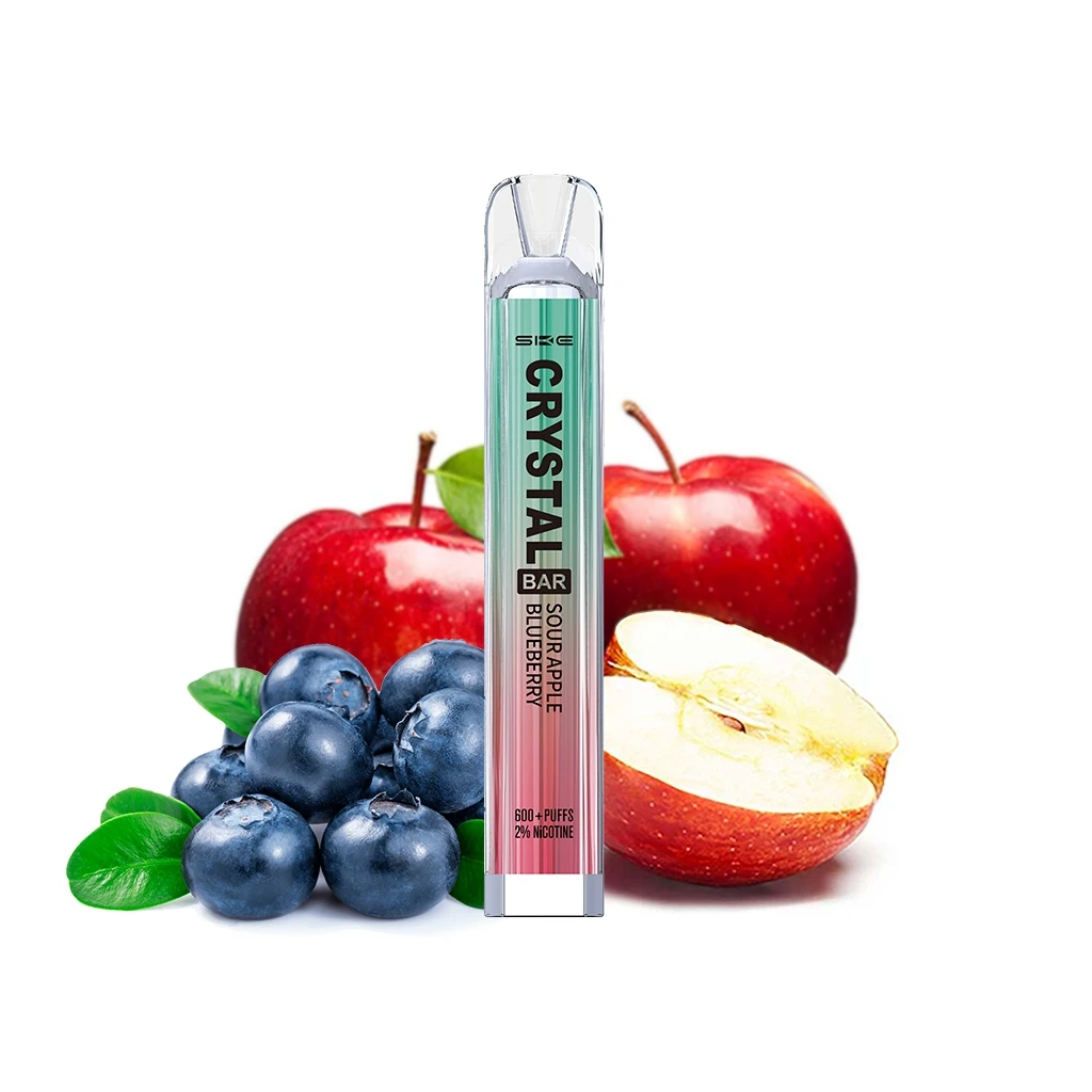 SKE Crystal Bar Sour Apple Blueberry de cuerpo verde y rosa con boquilla transparente, delante de manzanas rojas y arándanos. SKE Crystal Bar Sour Apple Blueberry de cuerpo verde y rosa con boquilla transparente, delante de manzanas rojas y arándanos.
