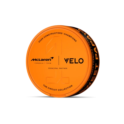 Lata circular naranja de VELO Sweet Papaya sobre fondo negro, vista en perspectiva, con logotipos de McLaren y VELO y un gran número 1 en relieve. Lata circular naranja de VELO Sweet Papaya sobre fondo negro, vista en perspectiva, con logotipos de McLaren y VELO y un gran número 1 en relieve.