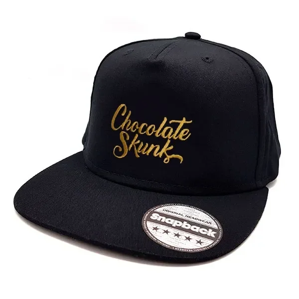 Gorra negra de visera plana con bordado dorado «Chocolate Skunk» en el frontal y pegatina circular sobre la visera.