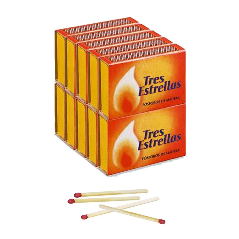 Cajas de fósforos Tres Estrellas apiladas, con diseño naranja y amarillo y una llama, junto a cerillas de madera con cabeza roja.