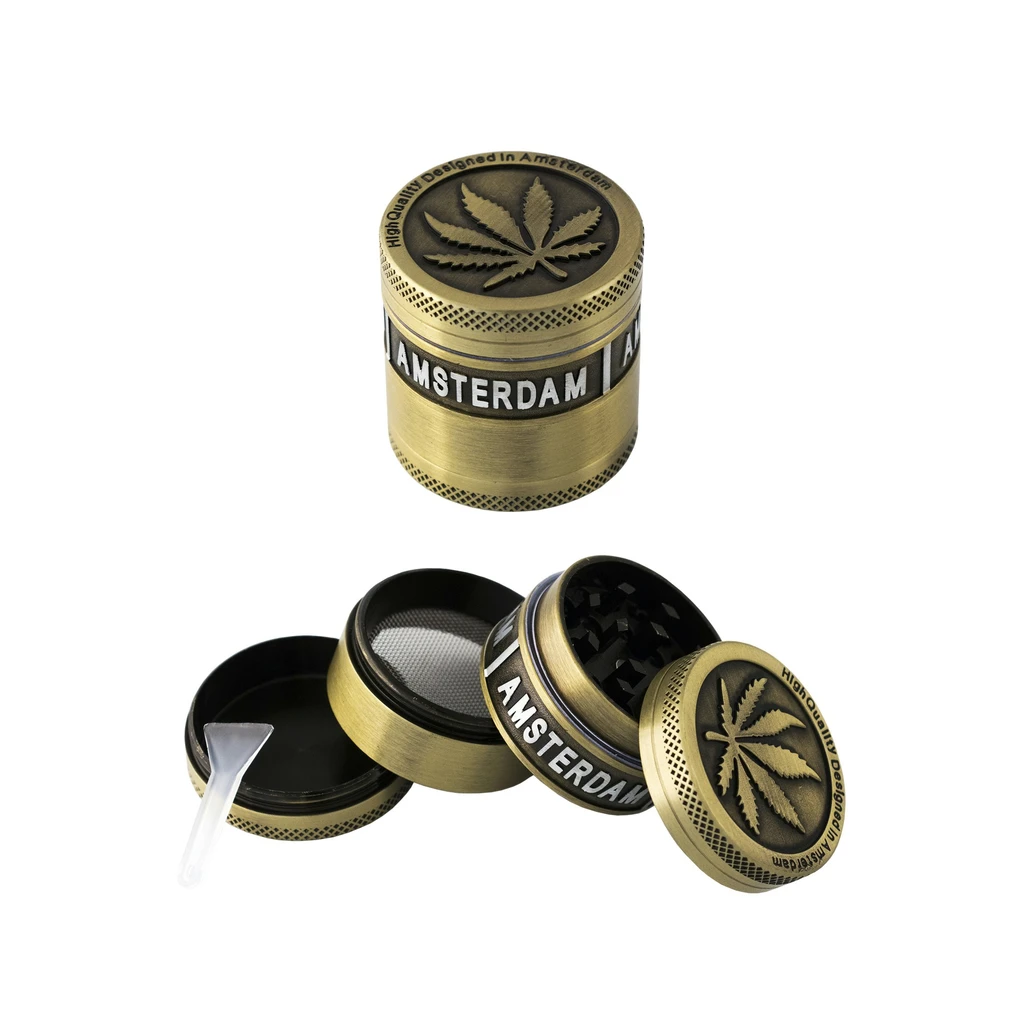 Grinder Amsterdam dorado, cerrado y desmontado, con hoja de cannabis en la tapa, dientes, malla y espátula.