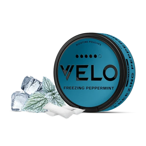 Envase redondo turquesa de VELO Freezing Peppermint junto a bolsas blancas, hojas de menta y cubitos de hielo sobre fondo negro.