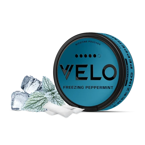 Envase redondo turquesa de VELO Freezing Peppermint junto a bolsas blancas, hojas de menta y cubitos de hielo sobre fondo negro.