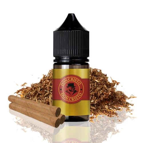 Frasco de aroma Don Cristo con tapón negro y etiqueta dorada y roja, acompañado de cigarros y hojas de tabaco desmenuzadas.