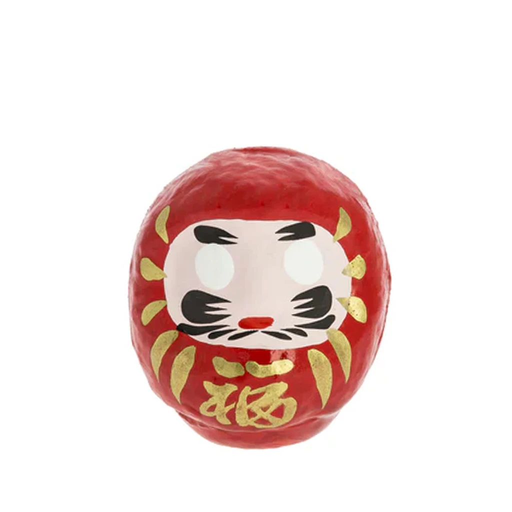 Daruma rojo de forma redondeada, con rostro blanco, cejas y bigote negros y adornos dorados, sobre fondo blanco. Daruma rojo de forma redondeada, con rostro blanco, cejas y bigote negros y adornos dorados, sobre fondo blanco.