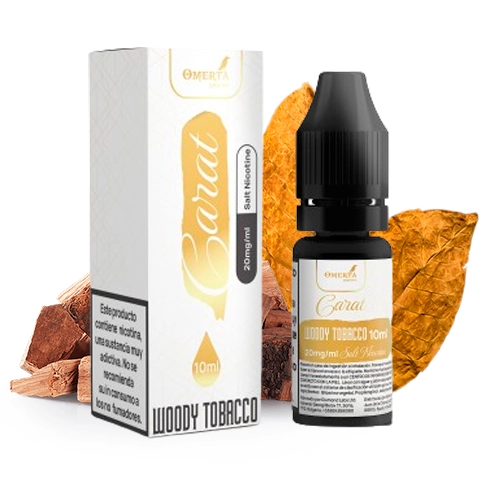 Frasco de Omerta Carat Salts Woody Tobacco con tapón negro y su caja blanca, junto a hojas de tabaco y trozos de madera.