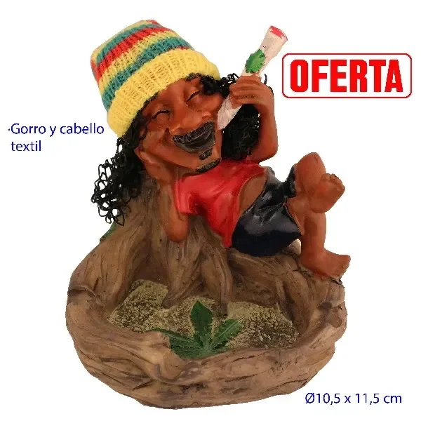Cenicero de mesa con figura rasta reclinada, gorro multicolor, cabello negro y camiseta roja sobre una base con hoja verde.