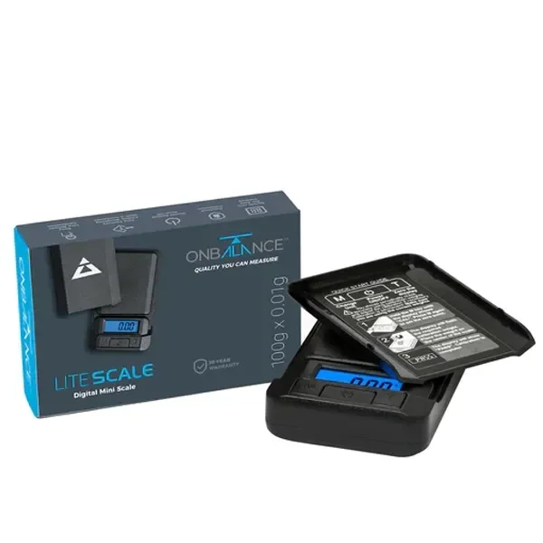 Báscula digital On Balance negra con pantalla azul y tapa levantada, junto a su caja con indicación de 100 g y 0,01 g.