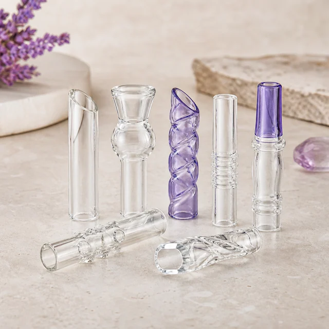 Siete boquillas de cristal transparentes y violetas, con formas lisas, curvas y en espiral, dispuestas de pie y tumbadas. Siete boquillas de cristal transparentes y violetas, con formas lisas, curvas y en espiral, dispuestas de pie y tumbadas.