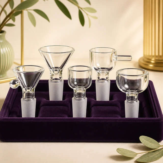 Cinco modelos de cazoletas de cristal transparente para bongs, con distintas formas, sobre una bandeja de terciopelo morado. Cinco modelos de cazoletas de cristal transparente para bongs, con distintas formas, sobre una bandeja de terciopelo morado.