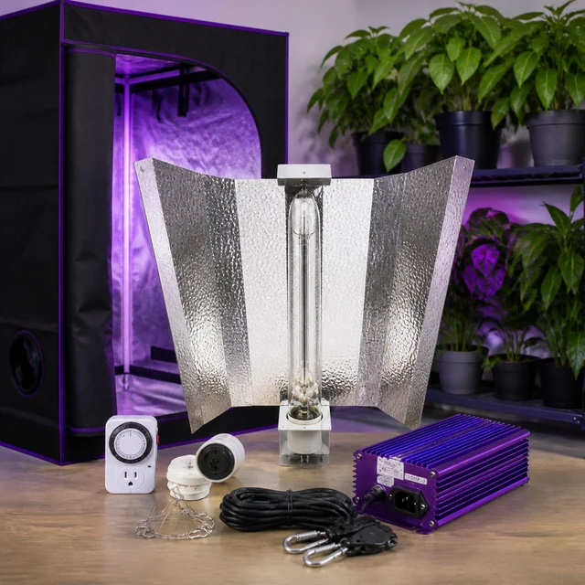 Equipo de iluminación con reflector, bombilla alargada, balastro morado, temporizador y cables, delante de un armario de cultivo. Equipo de iluminación con reflector, bombilla alargada, balastro morado, temporizador y cables, delante de un armario de cultivo.