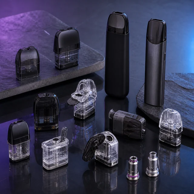 Dos dispositivos de vapeo junto a pods negros y transparentes de distintos formatos, algunos abiertos, y dos resistencias sobre una superficie oscura. Dos dispositivos de vapeo junto a pods negros y transparentes de distintos formatos, algunos abiertos, y dos resistencias sobre una superficie oscura.