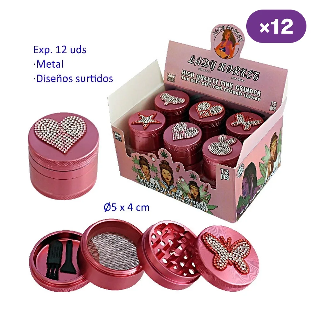 Grinders metálicos rosas en expositor, con corazones, estrellas y mariposas brillantes; uno desmontado muestra dientes, malla y raspadores.