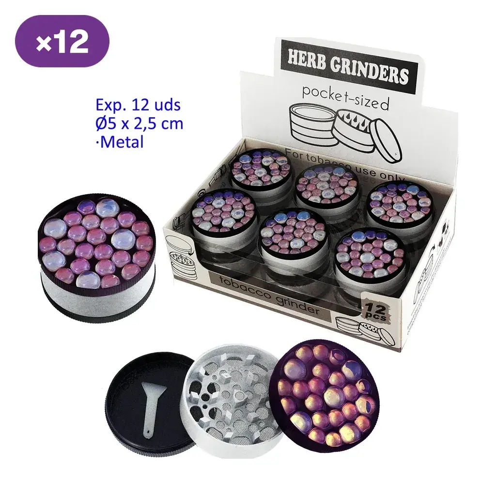 Expositor de grinders metálicos con tapas decoradas con círculos violetas y rosados; uno abierto muestra dientes, malla y una pequeña espátula.