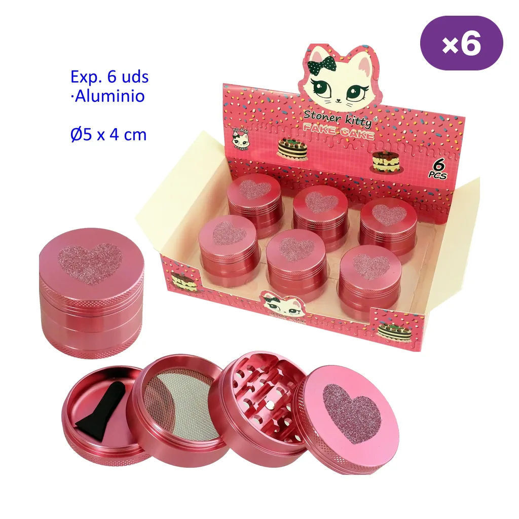Expositor con seis grinders rosas con corazones; delante, uno cerrado y otro desmontado en cuatro partes con dientes, malla y espátula.