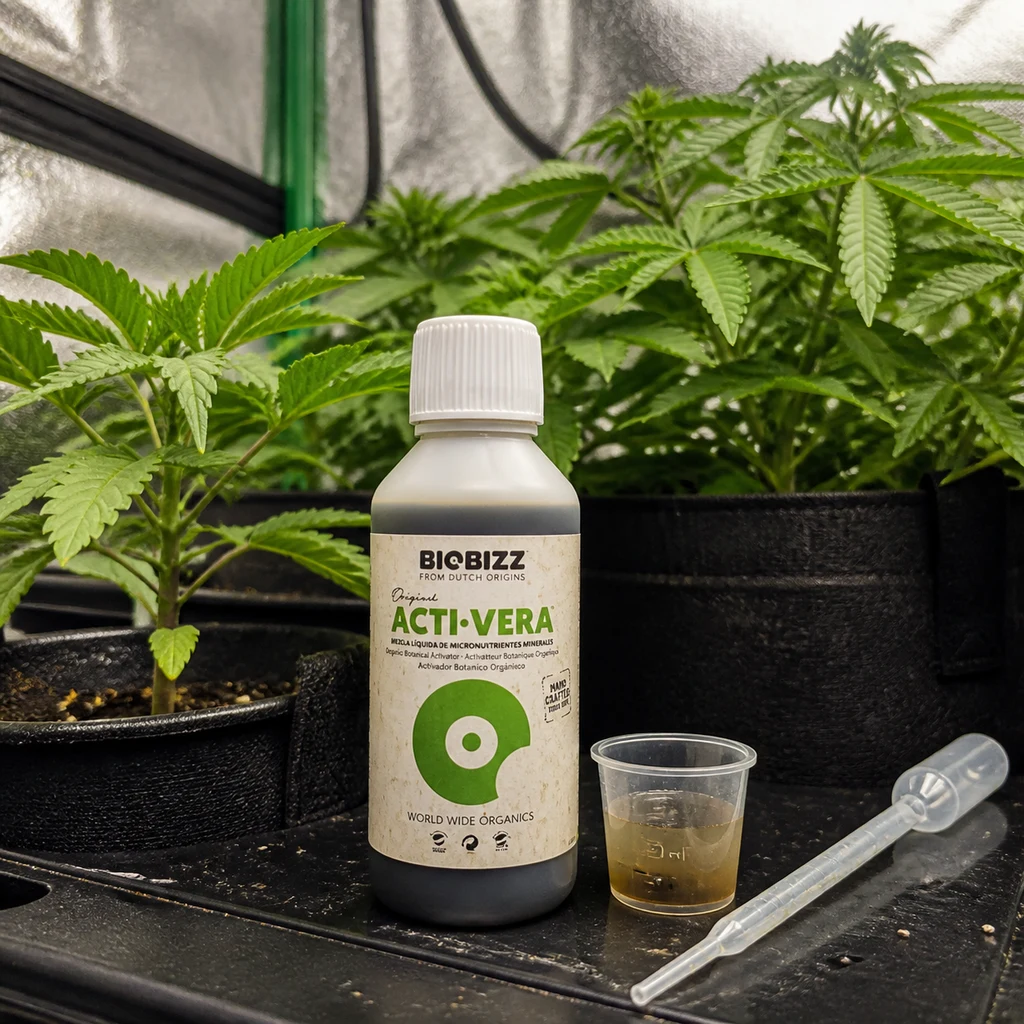 Bote de Acti-Vera BioBizz junto a un vaso dosificador con líquido y una pipeta, delante de plantas en macetas de tela.