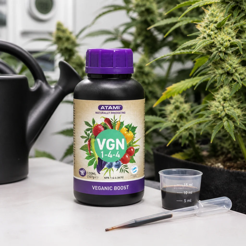 Bote Atami VGN 1-4-4 con tapón morado junto a un vaso dosificador y una pipeta, con regadera y plantas de cannabis al fondo.