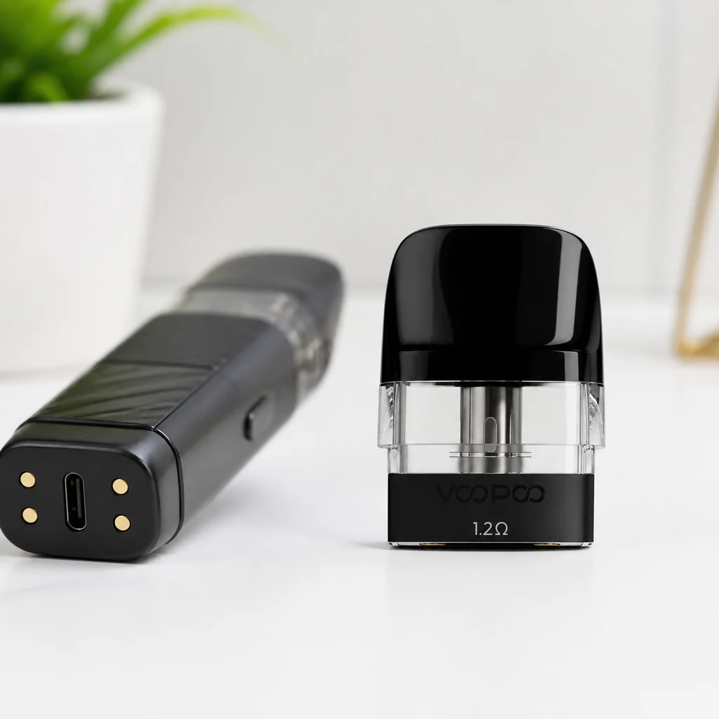 Cartucho Voopoo con boquilla negra, depósito transparente e inscripción de 1,2 Ω, junto a un dispositivo tumbado con puerto USB-C visible.