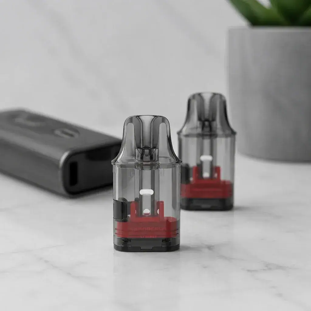 Pods Vaporesso Vibe translúcidos con boquilla oscura y base interior roja sobre una mesa, junto a un vapeador desenfocado.