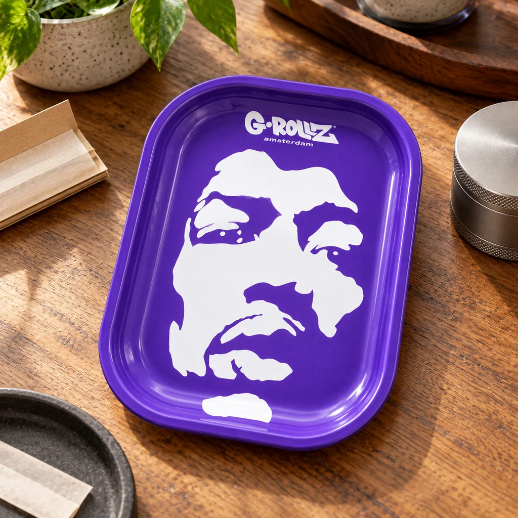 Bandeja de liar G-Rollz morada con un rostro blanco y bordes elevados, sobre una mesa de madera junto a papel de liar y un grinder.