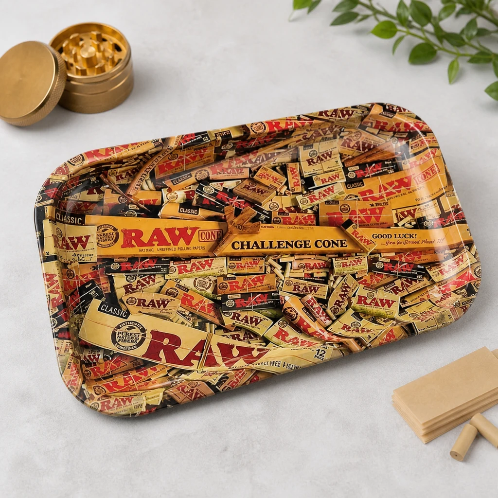 Bandeja RAW Mix con bordes elevados y un collage de diseños de la marca, sobre una mesa junto a un grinder dorado y papeles de liar.
