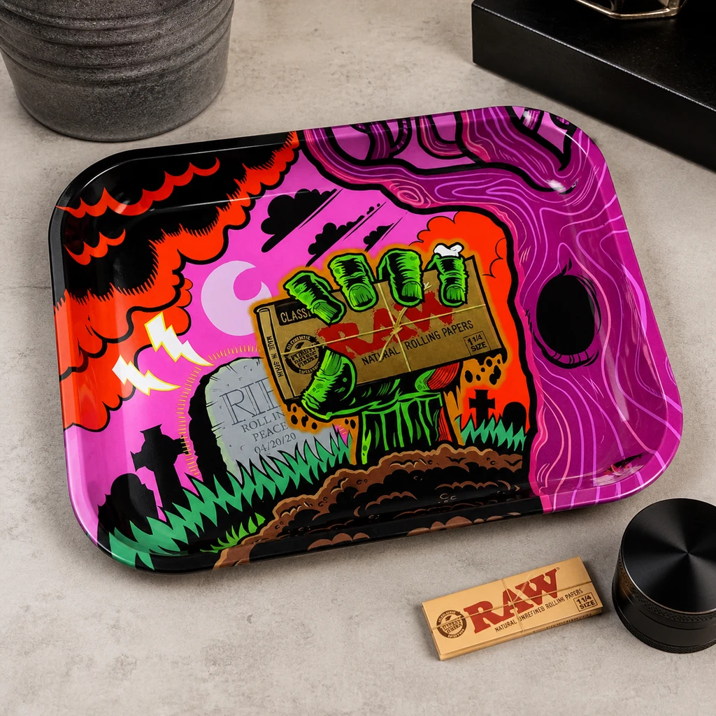 Bandeja RAW Zombie con dibujo de una mano verde sosteniendo papel de liar, junto a un librillo RAW y un grinder negro sobre una mesa.
