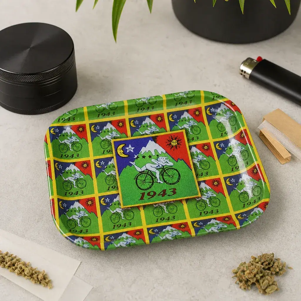 Bandeja de liar con estampado verde de un ciclista y el número 1943, sobre una mesa con grinder, mechero y papel de liar.