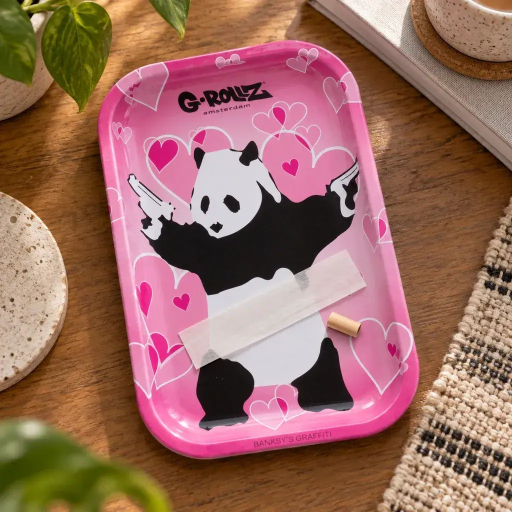 Bandeja rosa G-Rollz con corazones y un panda que sostiene pistolas, con papel de liar y una boquilla sobre una mesa de madera.