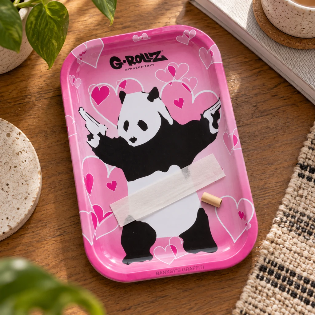 Bandeja rosa G-Rollz con corazones y un panda que sostiene pistolas, con papel de liar y una boquilla sobre una mesa de madera.