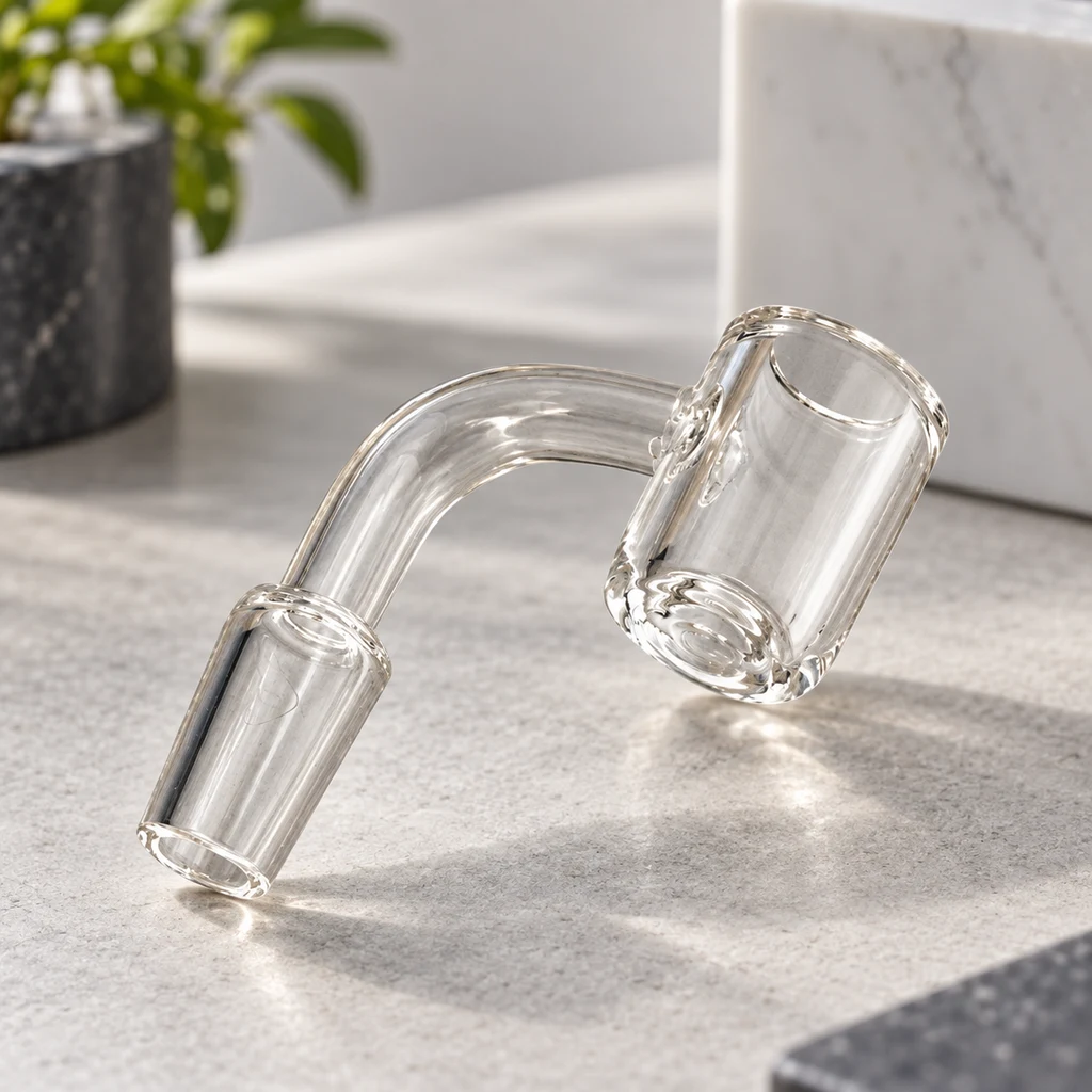 Banger de vidrio transparente con recipiente cilíndrico abierto, tubo curvado y conexión esmerilada, sobre una superficie gris.