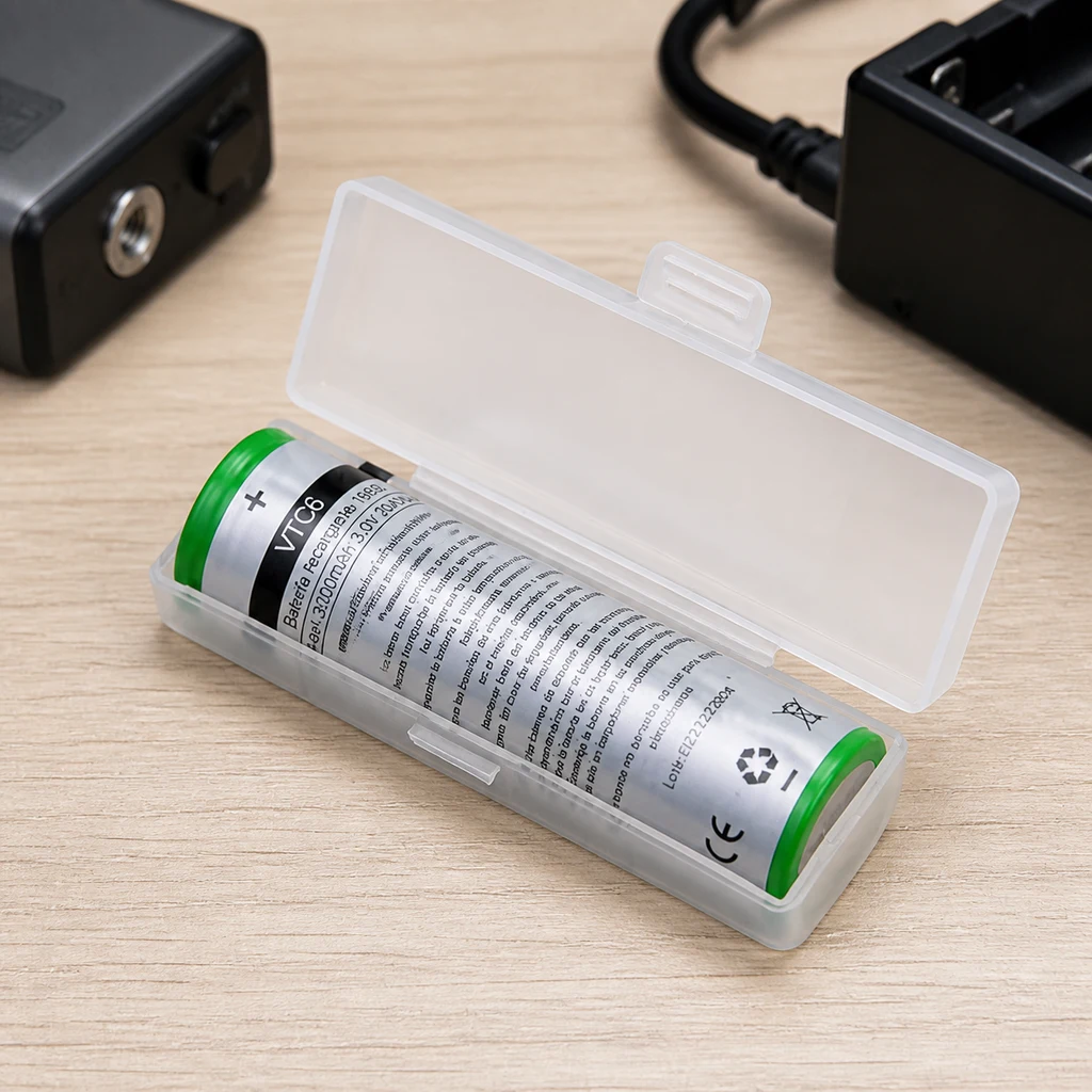 Batería recargable 18650 de 3000 mAh en un estuche translúcido abierto sobre una mesa, con un cargador negro al fondo.