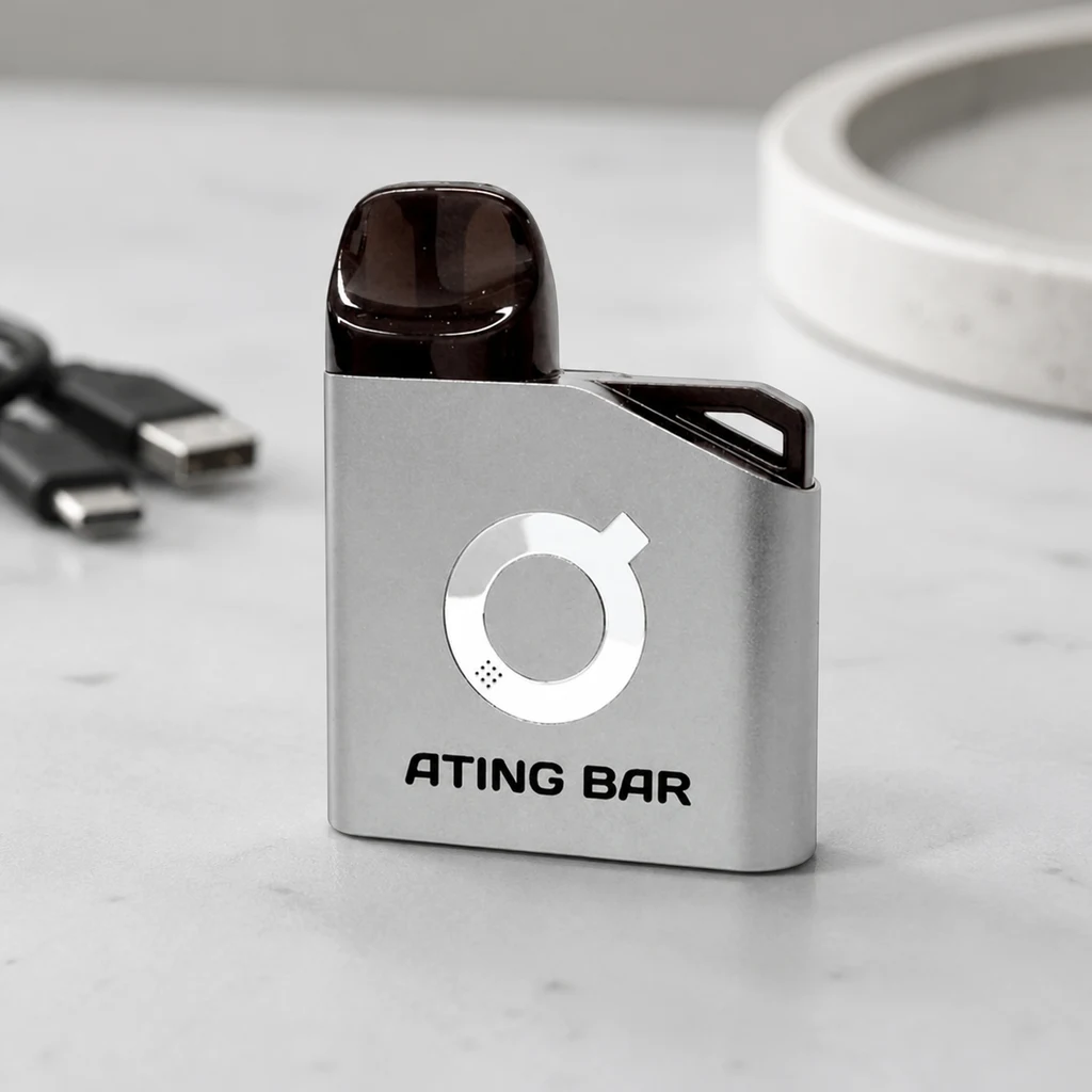 Pod Ating EVO-1 gris con boquilla oscura, logotipo circular y texto «ATING BAR», sobre una mesa con conectores USB al fondo.