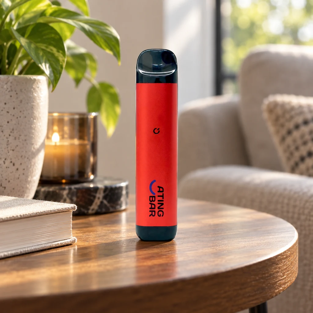 Batería Vape Ating EVO-2 roja con extremos oscuros, en vertical sobre una mesa de madera junto a un libro, una vela y una planta.