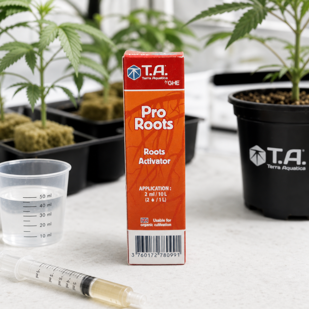 Caja naranja de Pro Roots de Terra Aquatica junto a un vaso graduado y una jeringa, con plantas de cannabis al fondo.