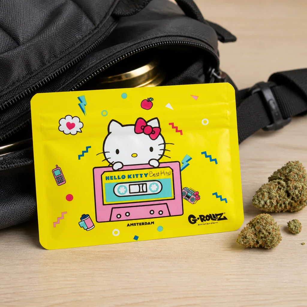 Bolsa amarilla G-Rollz con Hello Kitty sobre un casete rosa, apoyada junto a una mochila abierta y cogollos.