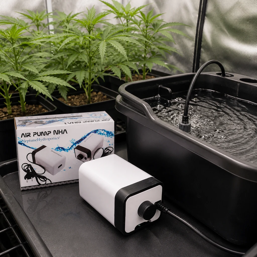Bomba de aire Neptune Hydroponics blanca y negra junto a su caja y un depósito con agua y burbujas, con plantas al fondo.