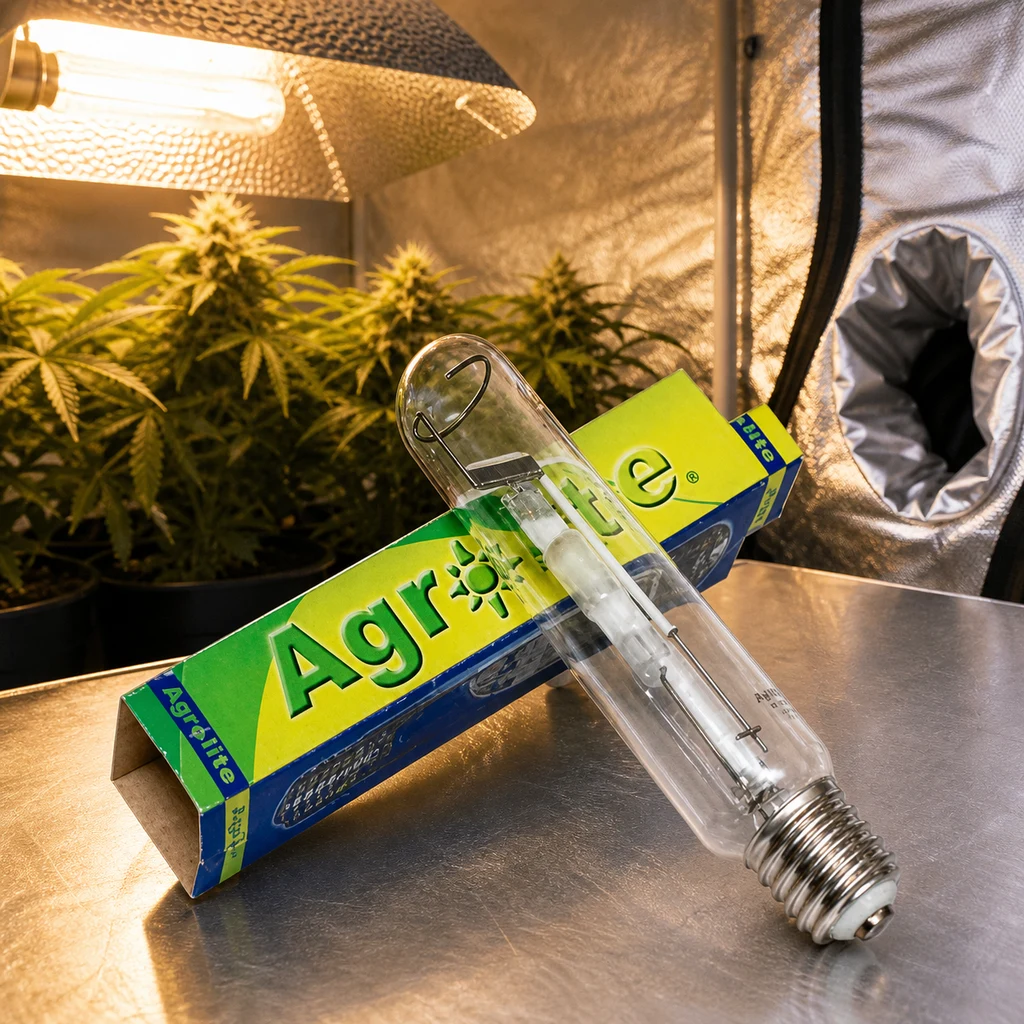 Lámpara Agrolite SHP Mixta con casquillo roscado apoyada sobre su caja, ante un armario de cultivo con plantas y un reflector iluminado.