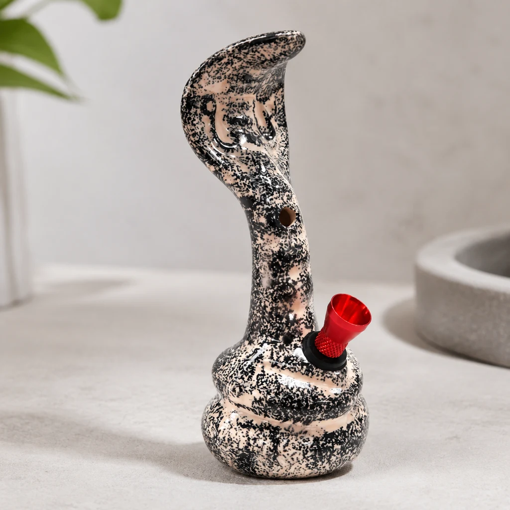Bong con forma de cobra erguida, acabado moteado negro y beige, orificio frontal y cazoleta roja lateral, sobre una mesa clara.
