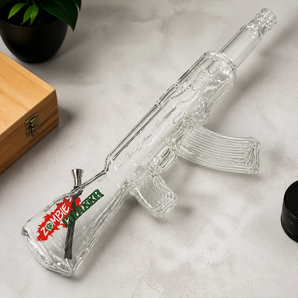 Bong de cristal transparente con forma de fusil AK-47, cazoleta metálica y texto «Zombie Killer», colocado en diagonal sobre una mesa.