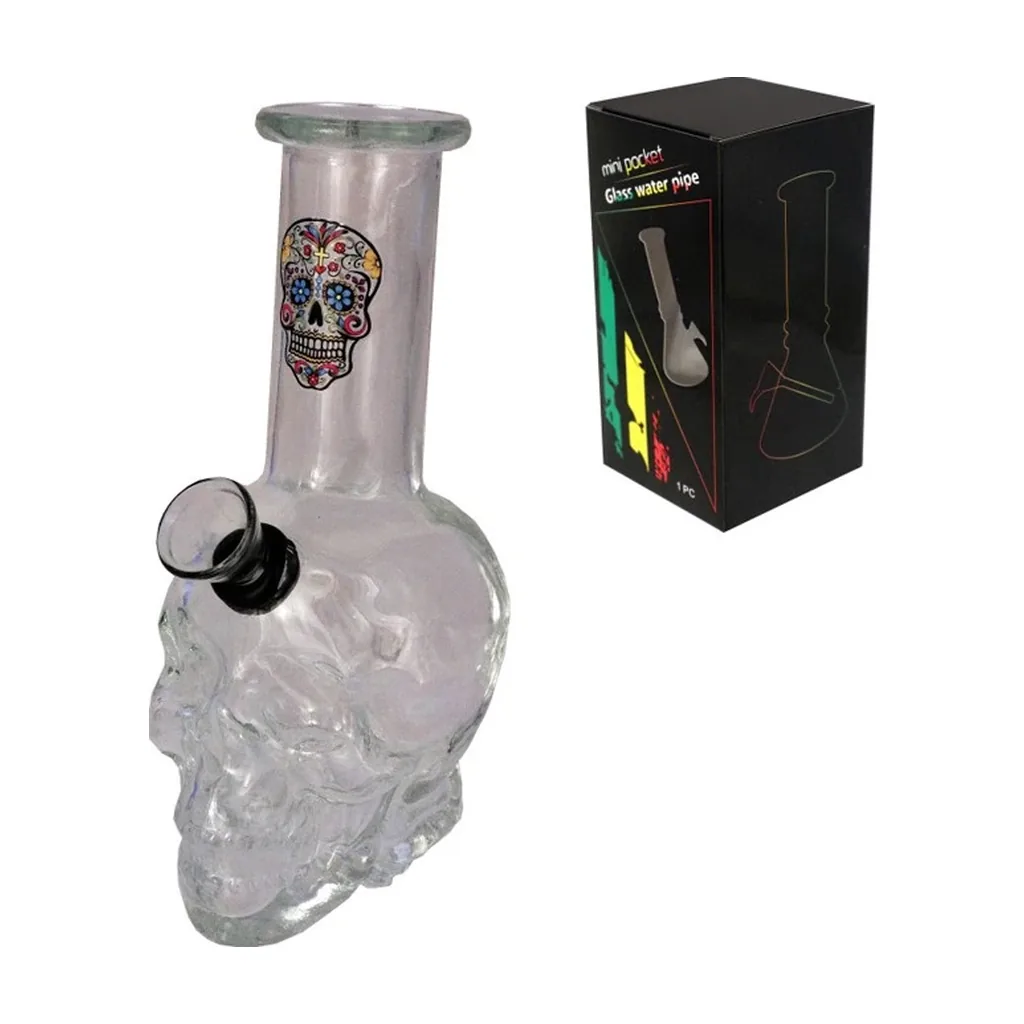 Bong de cristal transparente con base en forma de calavera, dibujo de Catrina en el cuello y cazoleta lateral, junto a su caja negra.