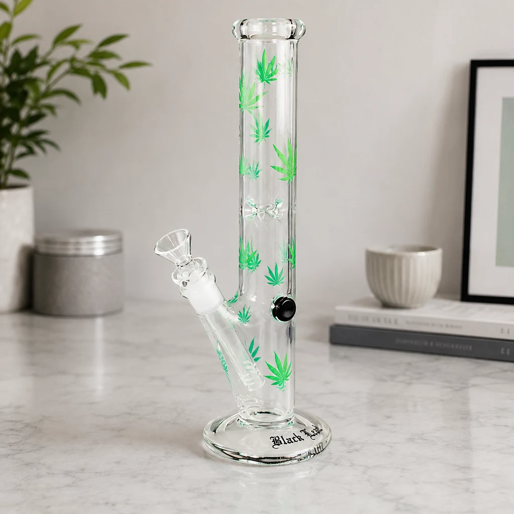 Bong Black Leaf transparente con hojas verdes estampadas, tubo recto, base circular y cazoleta lateral sobre una mesa clara.