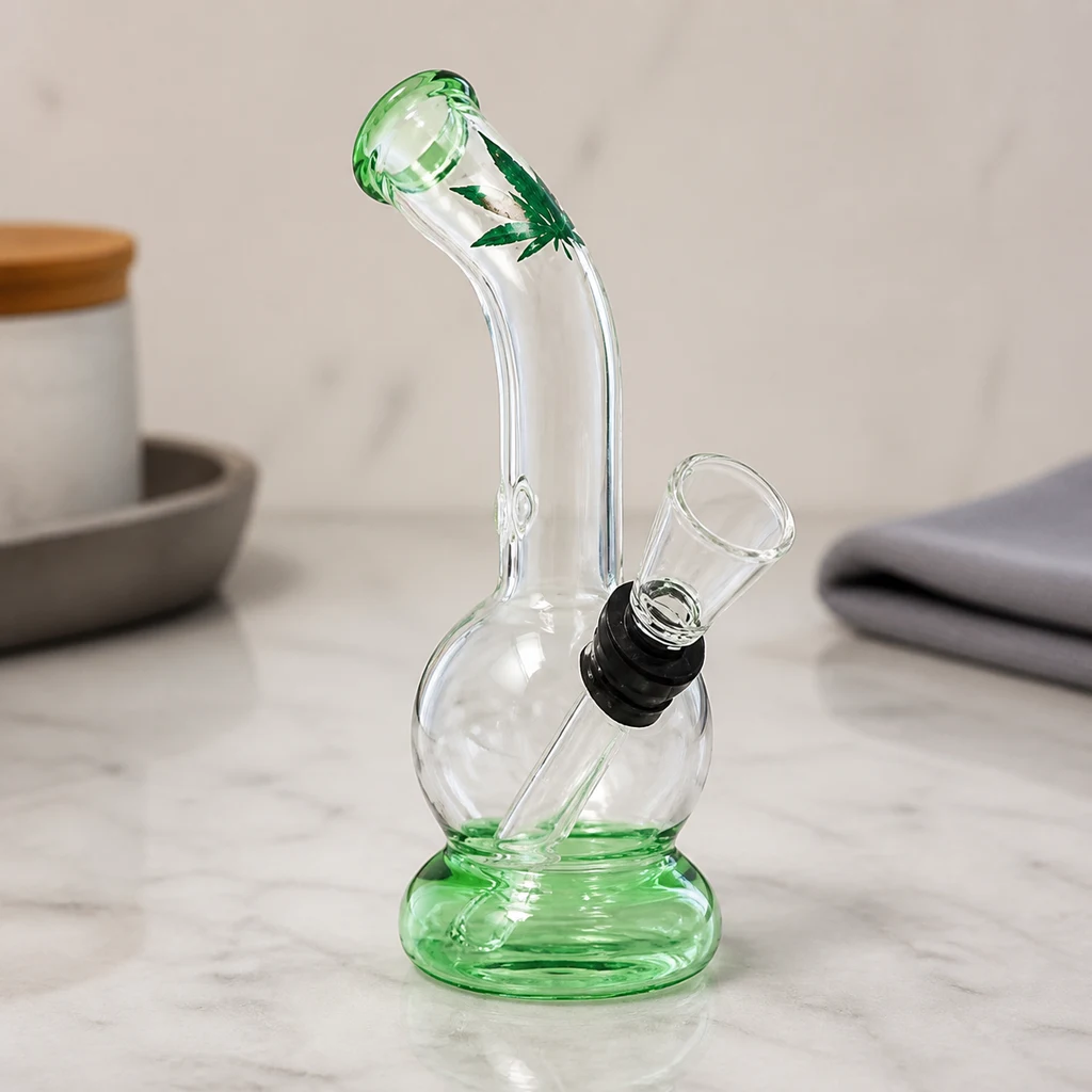 Bong Mini Crystal Leaf sobre una encimera, con cámara redonda transparente, base verde, cuello curvo y hoja verde decorativa.