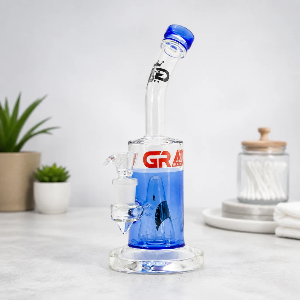Bong Shark Attack Grace Glass transparente y azul, con motivo de tiburón, cuello curvado y cazoleta lateral sobre una encimera.