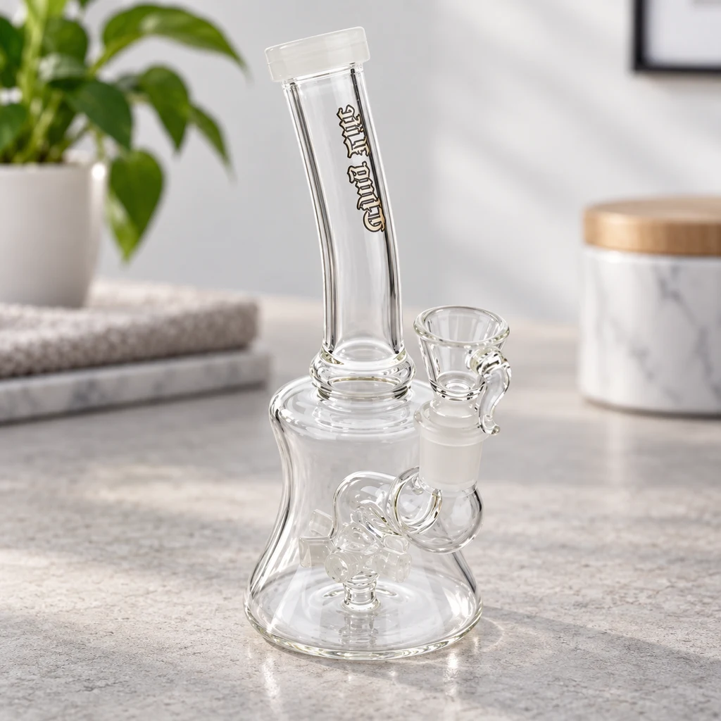 Bong transparente Thug Life con cuello curvado, cazoleta lateral y percolador visible, sobre una encimera junto a una planta.