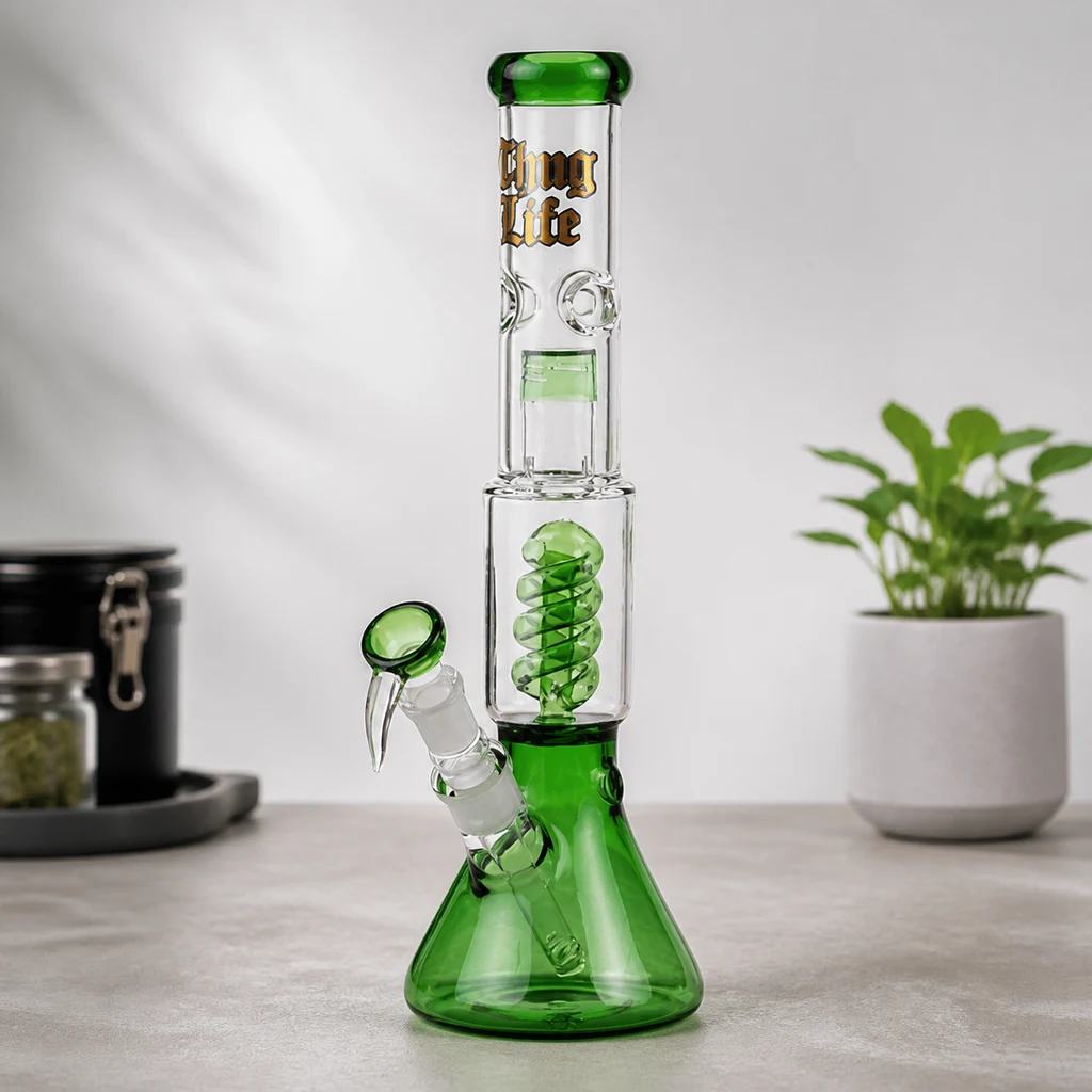 Bong Thug Life transparente y verde, con base ensanchada, espiral interior y cazoleta lateral, sobre una mesa junto a una planta.