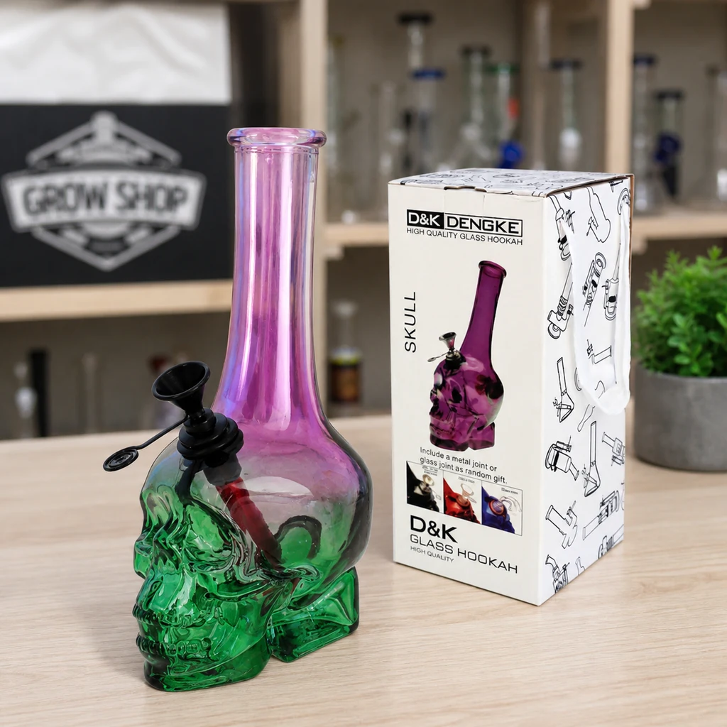 Escena generada de un bong con base de calavera verde y cuello violeta, junto a su caja sobre un mostrador.
